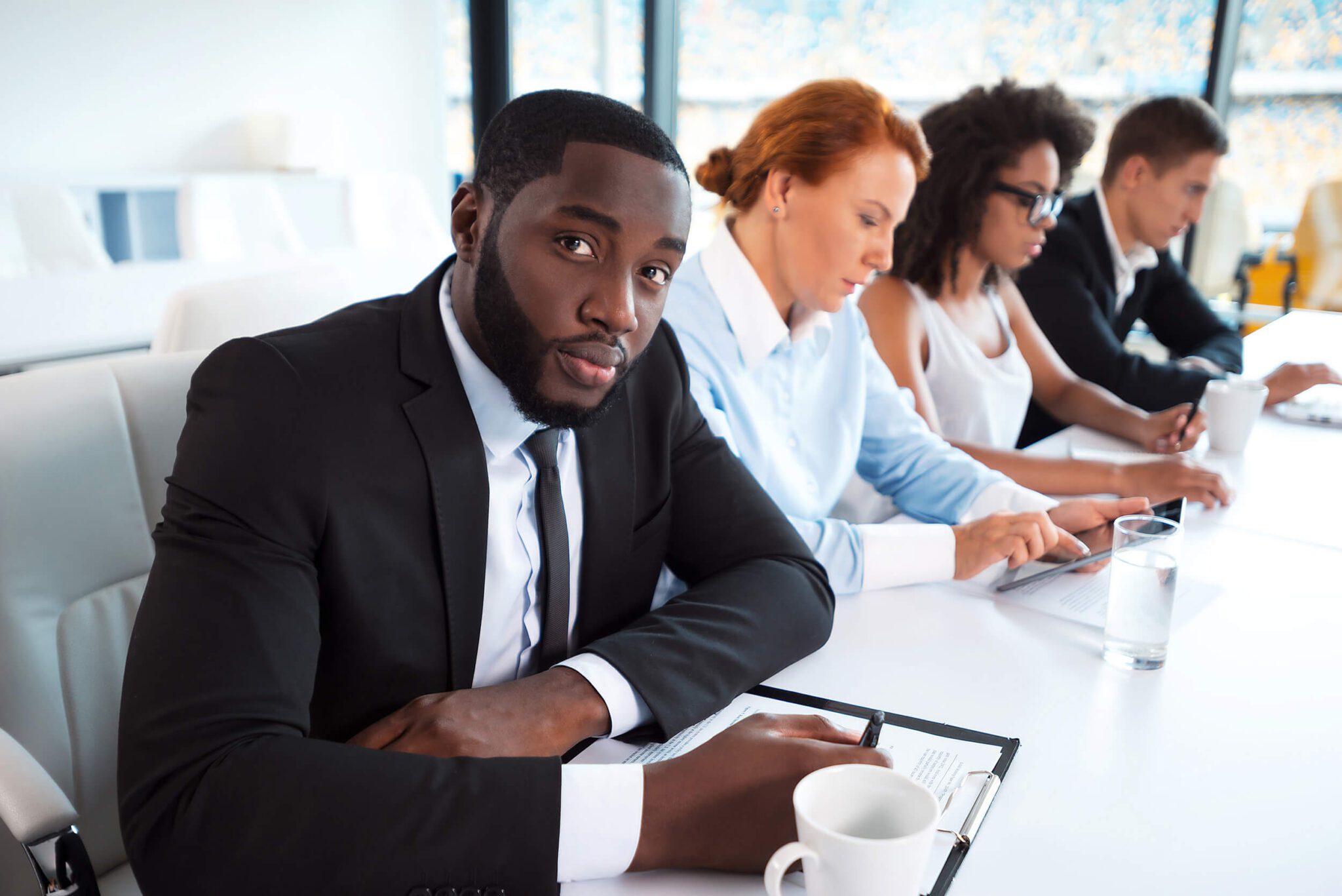 A black male employee is seated at a table with three other employees. He looks doubtful, as if he is failing to learn how to learn.